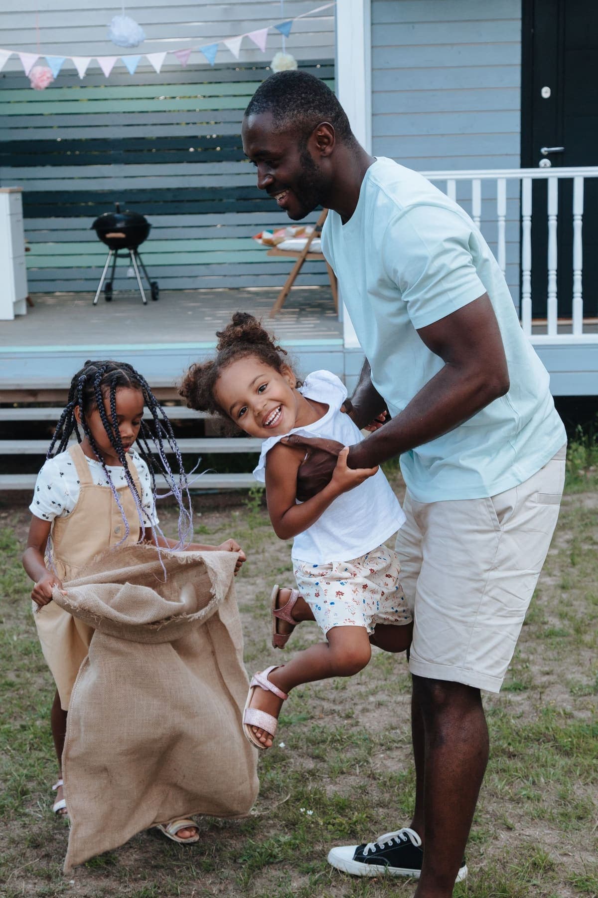 A dad and his daughters mid sack race in the yard