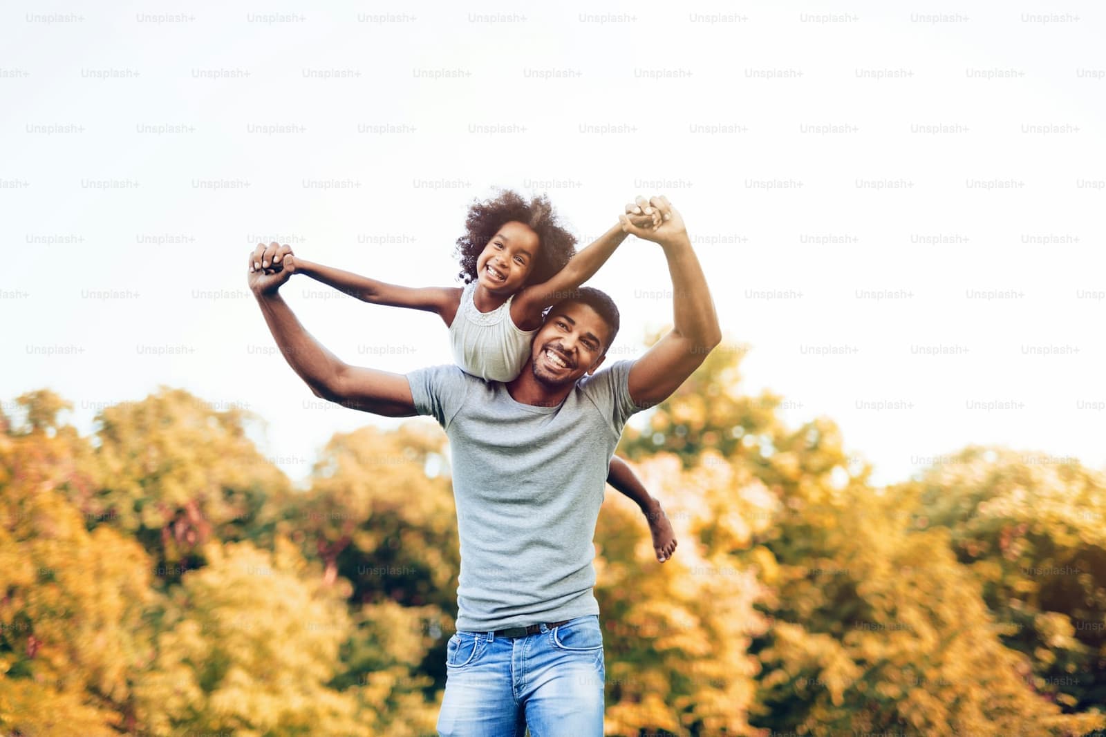 A father laughing with his daughter riding on his shoulders in an autumn park